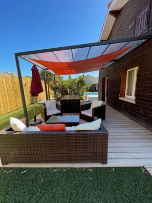 Eine Terrassengruppe mit Korbmöbeln, einem Glastisch und einem roten Sonnenschirm.