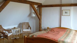 Une chambre confortable avec un lit en bois, deux fauteuils en osier, une petite table ronde et une lampe.