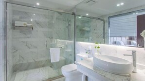 A modern bathroom with a glass-enclosed shower, a white toilet, a large oval sink, and a mirror.