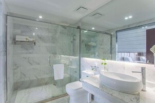 Un baño moderno con ducha envuelta en vidrio, inodoro blanco, un lavamanos ovalado grande y un espejo.