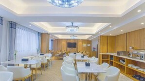 A hotel dining area with multiple tables and chairs, a chandelier, wooden paneling, and a television screen.