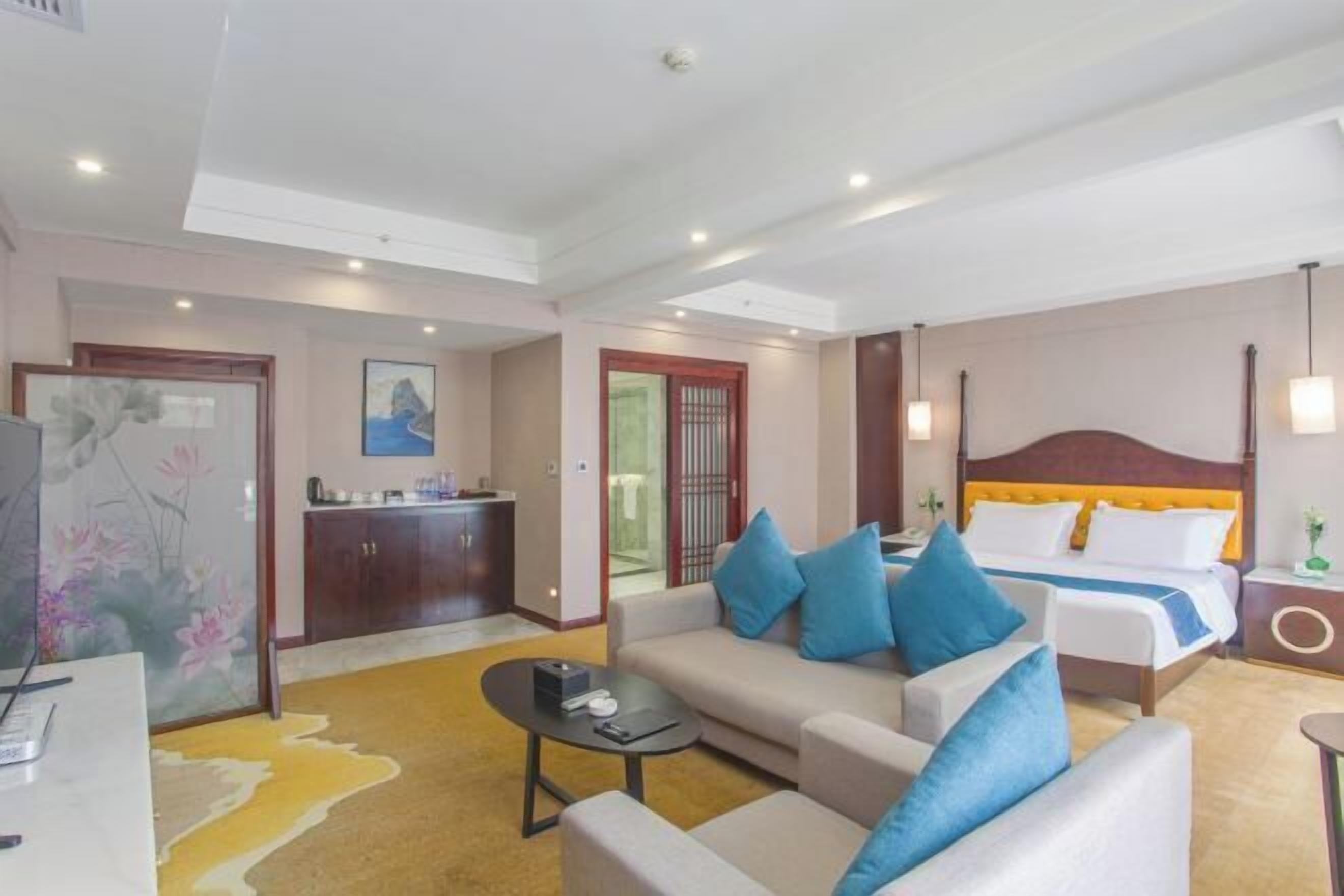 A hotel room with a sofa, a bed, a desk, and a kitchenette.