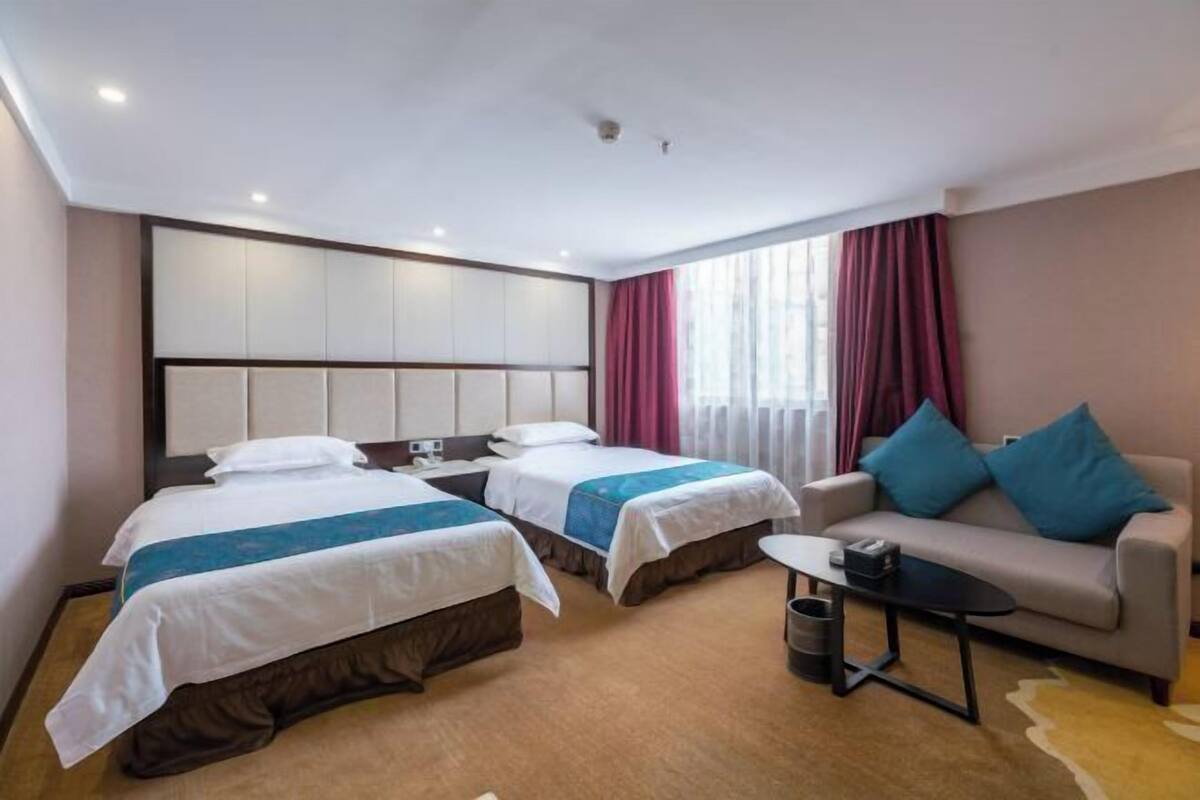 A hotel room with two beds, a sofa, a small table, and a trash bin.