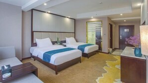 A hotel room with two beds, a desk, a chair, a nightstand, a lamp, and a window with blinds.
