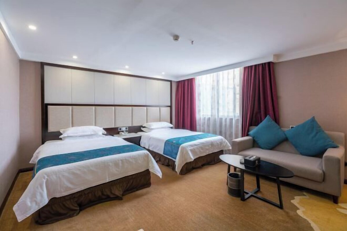 A hotel room with two beds, a sofa, a small table, and a trash bin.