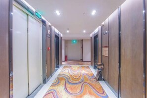 Un pasillo de hotel con alfombra estampada, puertas de madera y un cartel que indica la dirección al ascensor.