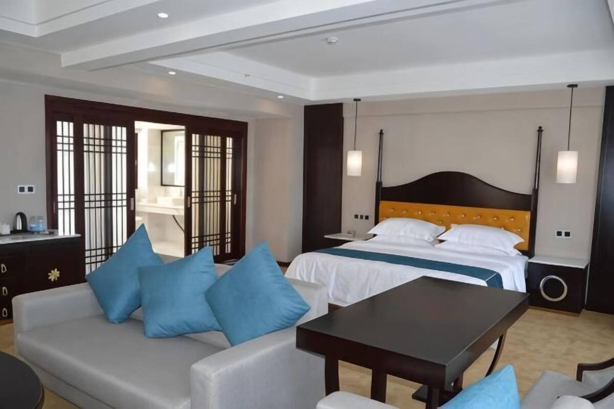 A hotel room with a bed, a sofa, a table, a dresser, and a view of the outside.