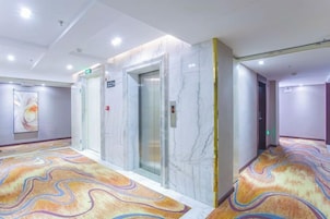 Un pasillo de hotel con paredes de mármol, un ascensor y una alfombra estampada.
