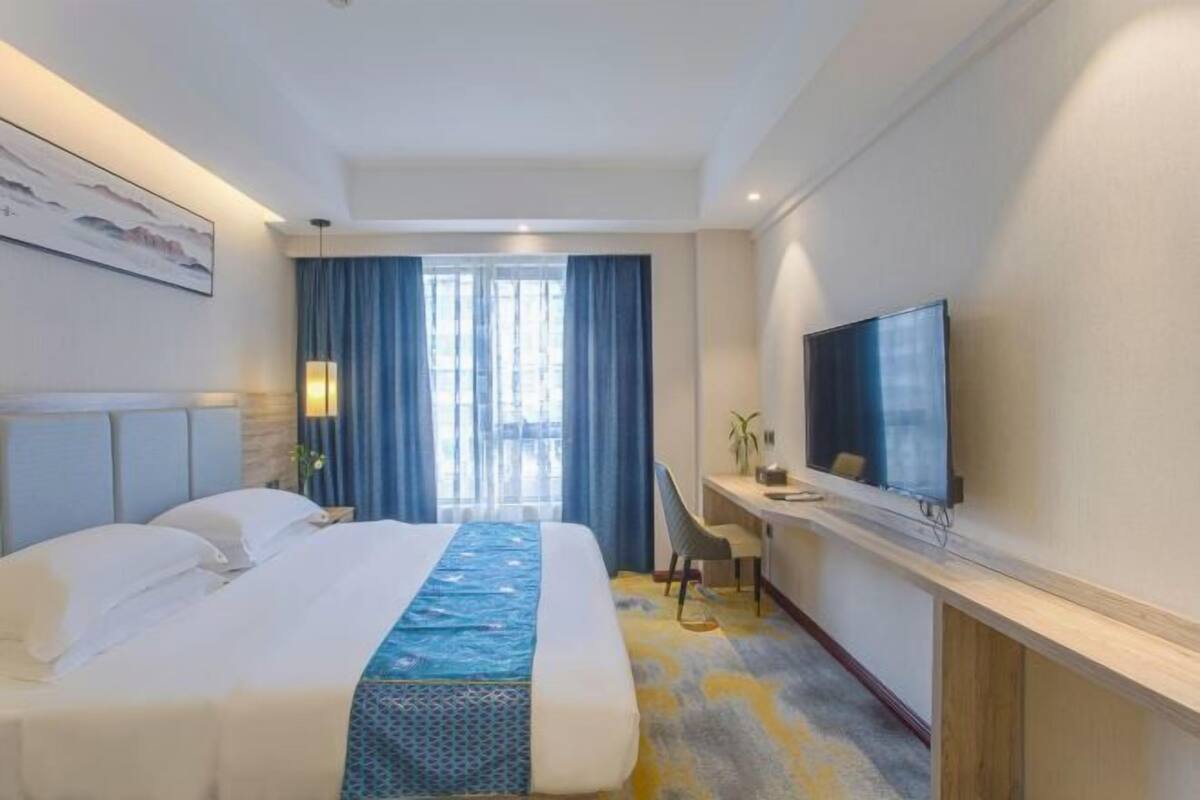 A hotel room with a large bed, a desk with a chair, a television, and a window with curtains.