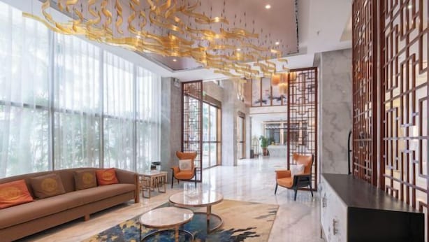 A modern hotel lobby with a sofa, round tables, and a decorative ceiling.