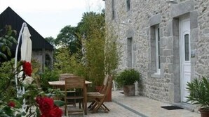 A stone building with a tiled patio, a wooden table and chairs, and potted plants. - Old farmhouse in Montchaton Orval sur sienne near Mont Saint Michel (Montchaton Orval sur sienne)