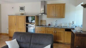 A compact kitchen with wooden cabinets, a built-in oven, and a stainless steel range hood. - Old farmhouse in Montchaton Orval sur sienne near Mont Saint Michel (Montchaton Orval sur sienne)