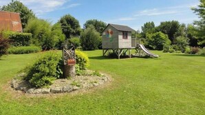 A wooden playhouse with a slide, surrounded by a well-maintained lawn and trees. - Old farmhouse in Montchaton Orval sur sienne near Mont Saint Michel (Montchaton Orval sur sienne)