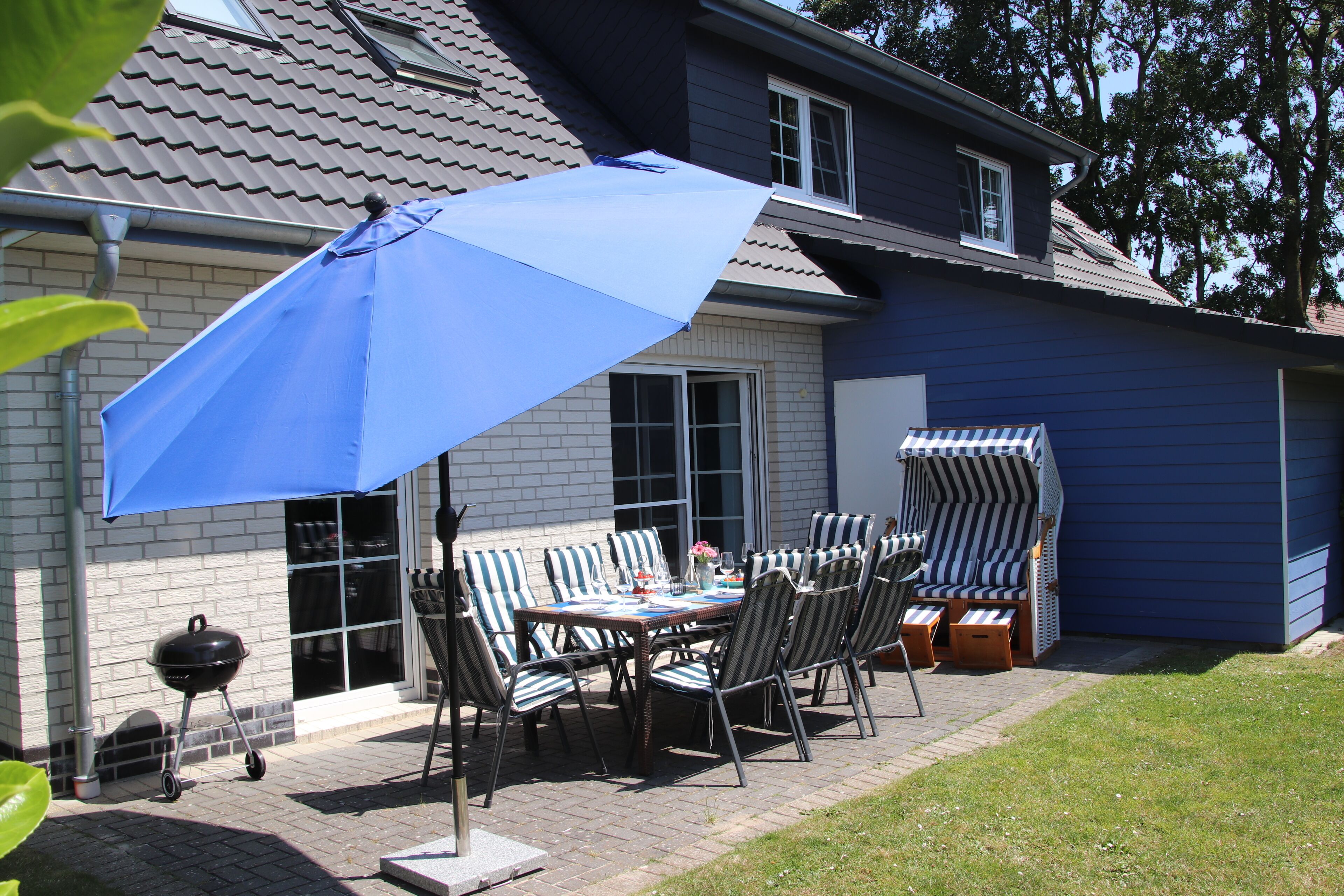 A patio with a table and chairs, a barbecue grill, and a blue umbrella.