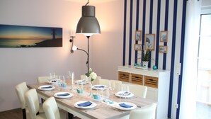 A dining area with a long table set for six, white chairs, and a modern pendant light. - Luxurious FH near the dike, sauna, fireplace, garden, beach chair (8 adults & baby) (Butjadingen)