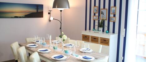 A dining area with a long table set for six, white chairs, and a modern pendant light.