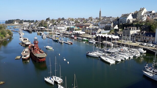 A marina with various boats docked, a prominent red ship, and buildings in the background. - Charming country home (Plogonnec)