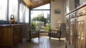 A cozy kitchen with wooden cabinets, a dining table, and chairs. There is a window with blinds, a potted plant, and a painting on the wall. - Charming country home (Plogonnec)