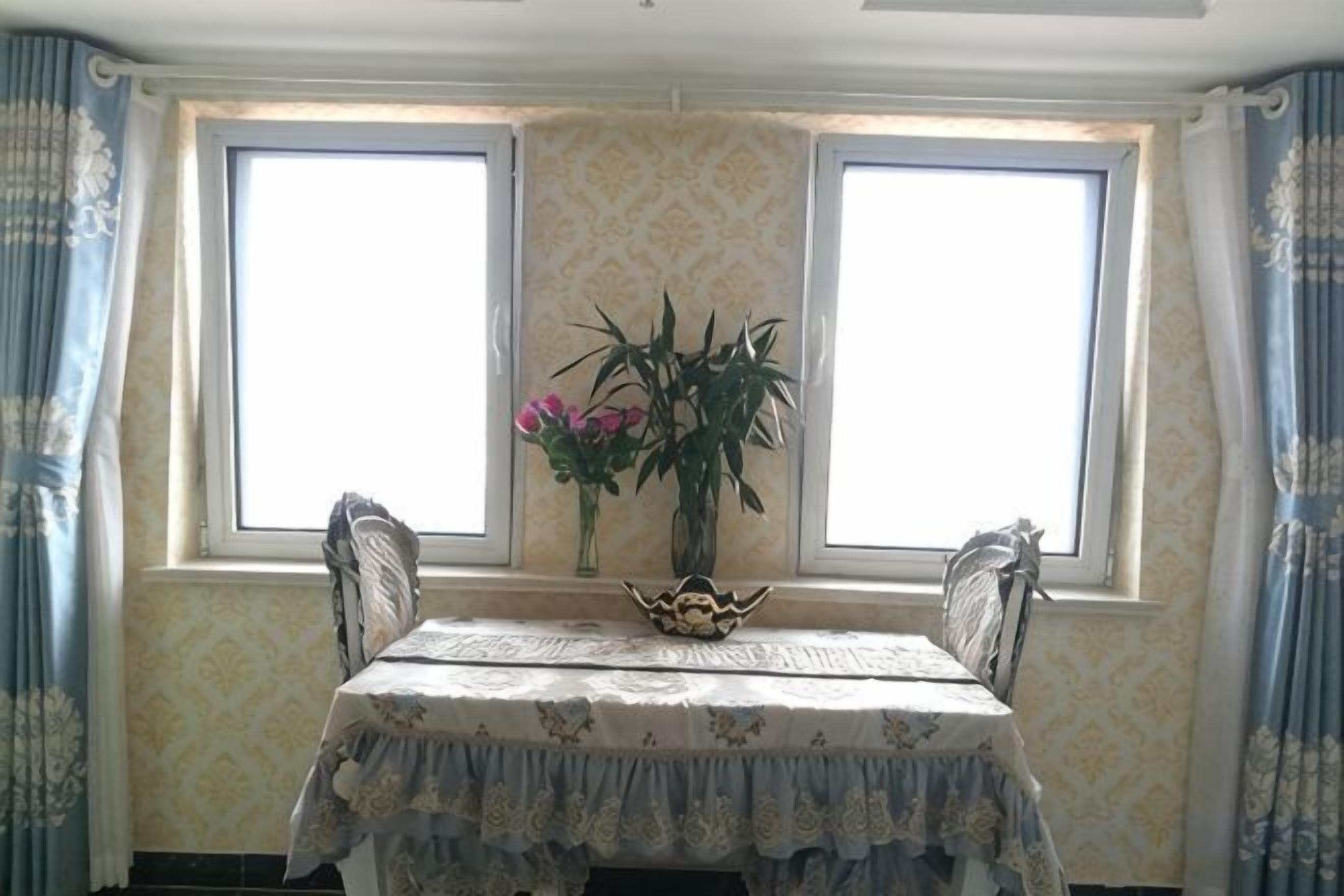 A dining table with a floral tablecloth, two chairs, and a vase with flowers.