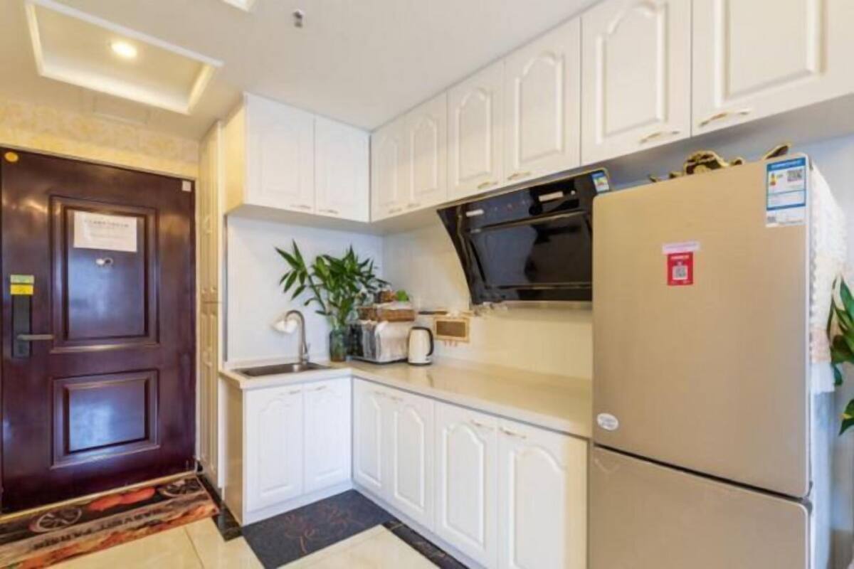 Una cocina compacta con muebles blancos, un microondas, un refrigerador y un lavamanos pequeño.