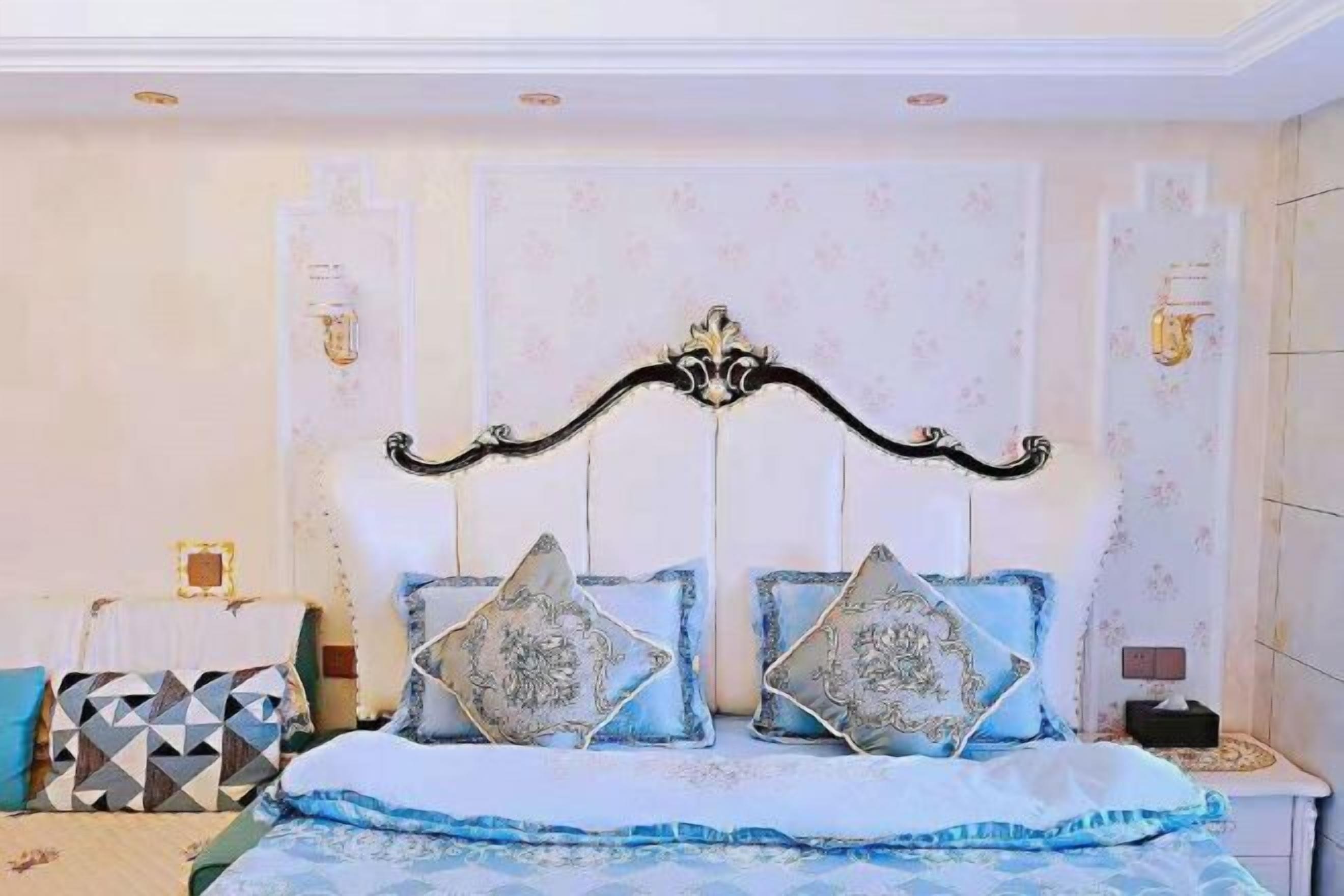 A bedroom with a bed, decorative pillows, a nightstand, and wall sconces.