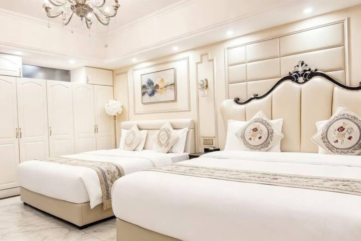 Habitación de hotel con dos camas, una araña, un cuadro en la pared y un armario grande.