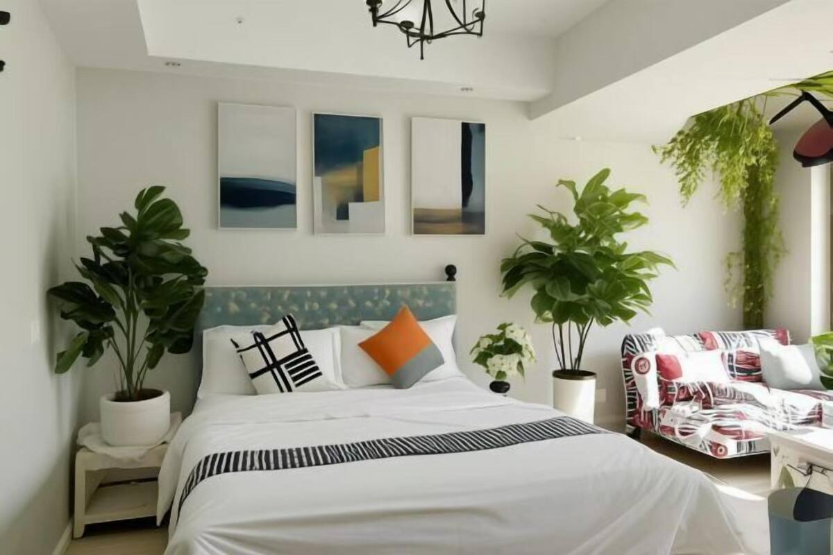 Un dormitorio con una cama, dos plantas en macetas, un sofá y tres obras de arte colgadas en la pared.