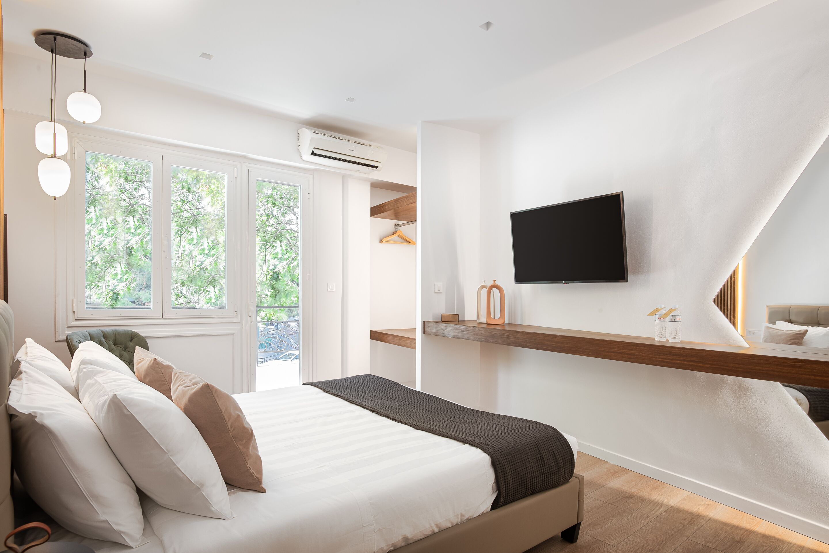 Un dormitorio moderno con cama, mesitas de noche, televisor y ventana con vista a follaje.