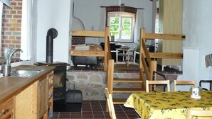 Une cuisine rustique avec un mur en briques, des poutres en bois, un poêle et une fenêtre agrémentée de rideaux.