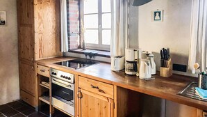 Une cuisine avec des meubles de rangement en bois, un four encastré, un évier et une fenêtre avec des rideaux.
