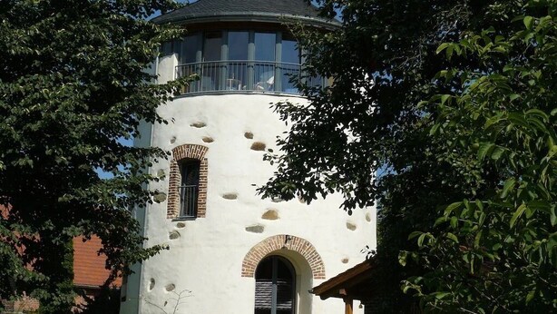 Une tour blanche dotée d  ’un balcon, de fenêtres en arc de cercle et d’une entrée en briques.