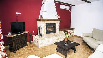 Ein Wohnzimmer mit Kamin aus Stein, einem Fernseher auf einem Schrank, einer Couch und einem Couchtisch.
