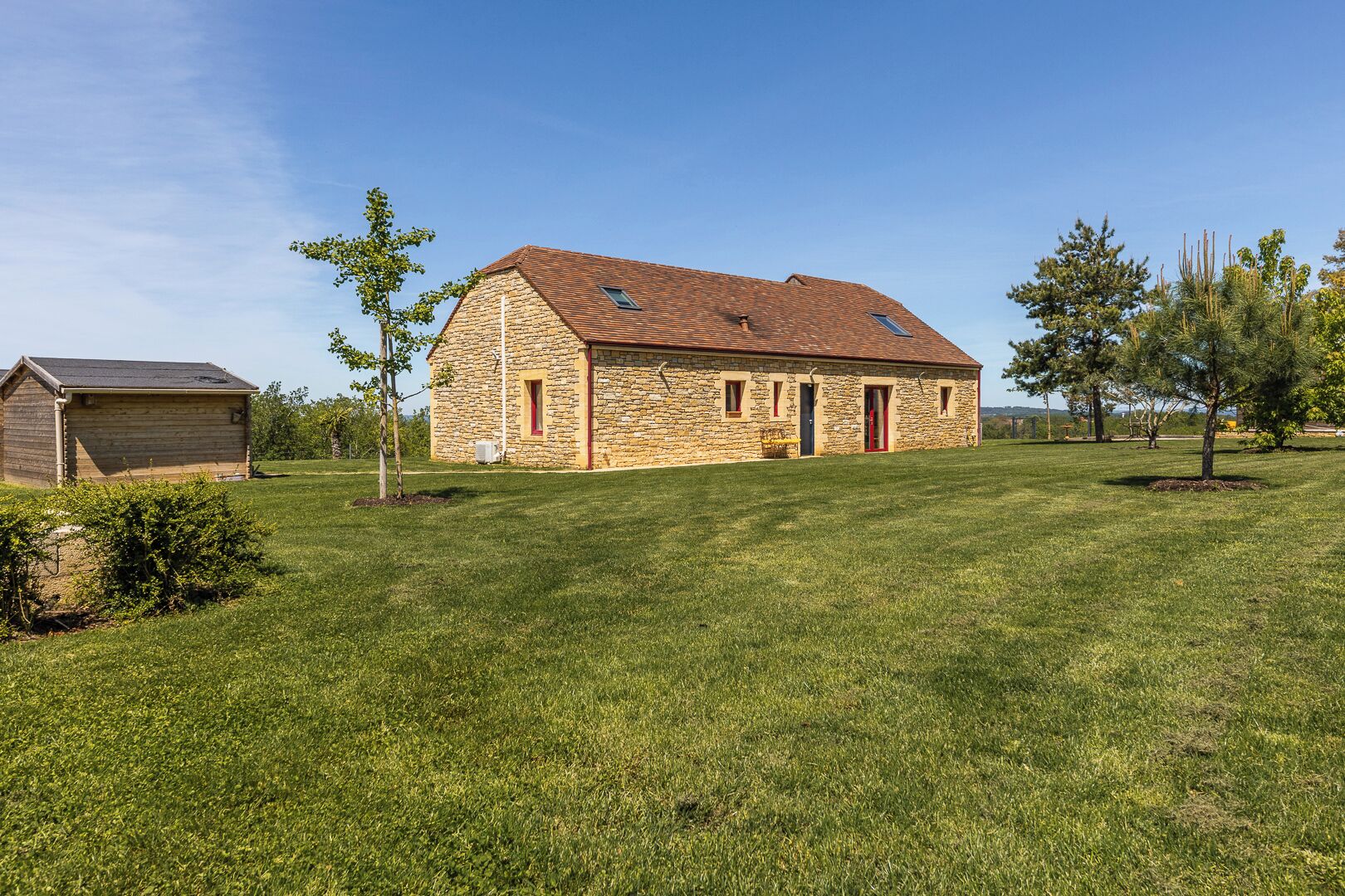 A stone building with a sloped roof, a small attached structure, and a well-maintained grassy lawn.