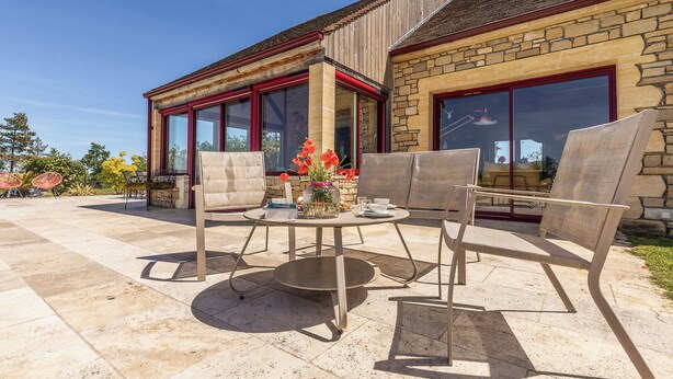 An outdoor patio with a round table and four chairs, a vase with flowers, and a stone building with large windows and a red roof. - Trufièra, a lovely holiday house (Florimont-Gaumier)