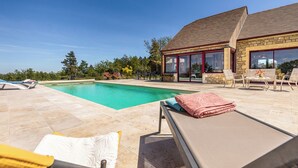 A poolside area with lounge chairs, a stone building with large windows, and a clear blue sky. - Trufièra, a lovely holiday house (Florimont-Gaumier)
