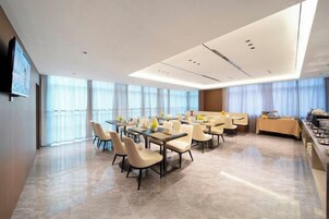 Un salón de conferencias moderno en un hotel, con varias mesas y sillas, ventanas amplias y un televisor de pantalla plana en la pared.