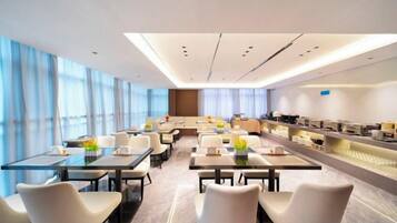 A modern hotel conference room with tables, chairs, and a kitchen area.