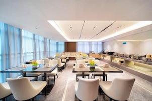 A modern hotel conference room with tables, chairs, and a kitchen area.