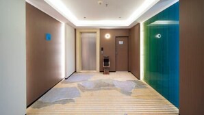 Un pasillo de hotel con piso alfombrado, una puerta con un letrero y un muro de vidrio verde.