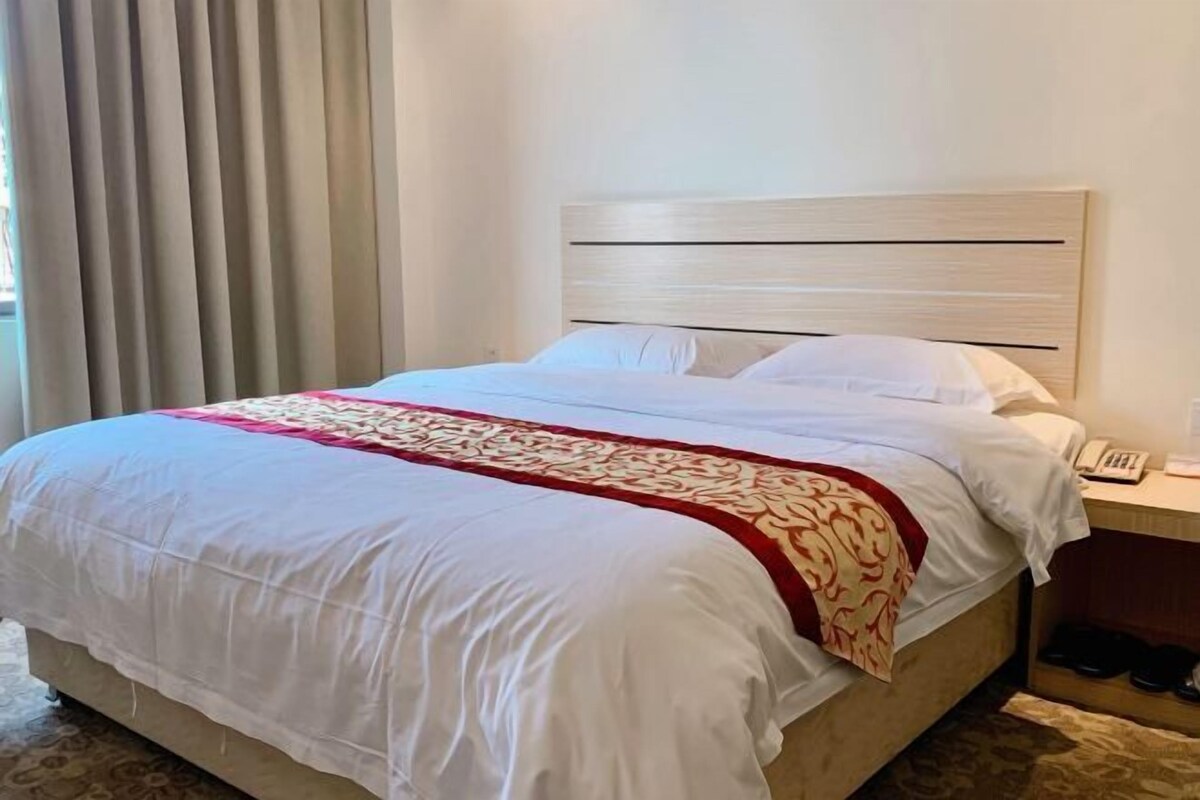 A hotel room with a bed, a bedside table with a phone, and a pair of shoes on the floor.