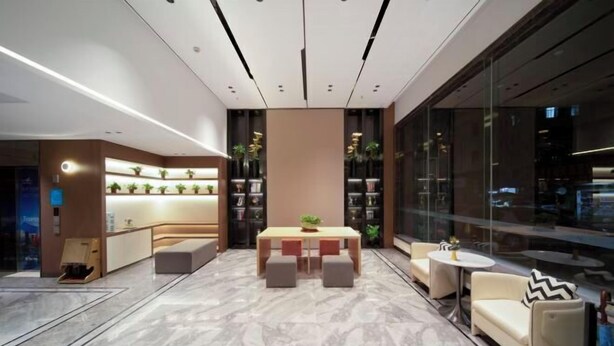 Un vestíbulo moderno con piso de mármol, una mesa central con asientos y un muro de cristal con vista a la ciudad.