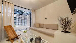 Een moderne woonkamer met een bank, een houten stoel, een glazen salontafel en een potplant.