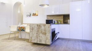 Une cuisine moderne avec des meubles blancs, un four encastré et un coin repas comprenant une table et des chaises.