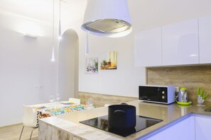A modern kitchen with white cabinets, a microwave, a kettle, and a dining area with a table set for two.