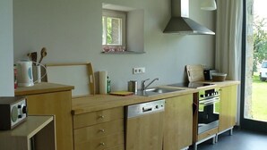 Une cuisine compacte dotée de meubles en bois, d’un lave-vaisselle encastré, d’une cuisinière et d’une fenêtre laissant entrer la lumière naturelle.