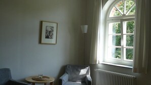 Une pièce dotée d’une grande fenêtre en arc de cercle, d’un radiateur, d’un tableau encadré accroché au mur et de deux chaises.