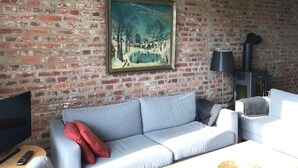 Un salon avec un mur en briques, un tableau, un canapé, un téléviseur et une cheminée.