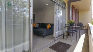 A modern living room with a dark sofa, a glass door leading to an outdoor area, and a small table with chairs.
