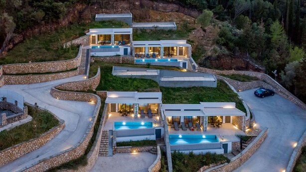 Une maison moderne à plusieurs étages, dotée d’une piscine, de murs de soutènement en pierre et d’une allée sinueuse.