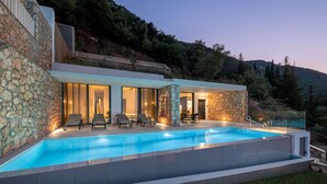 Une maison moderne dotée d’une piscine, de murs en pierre et offrant une vue sur les collines environnantes.